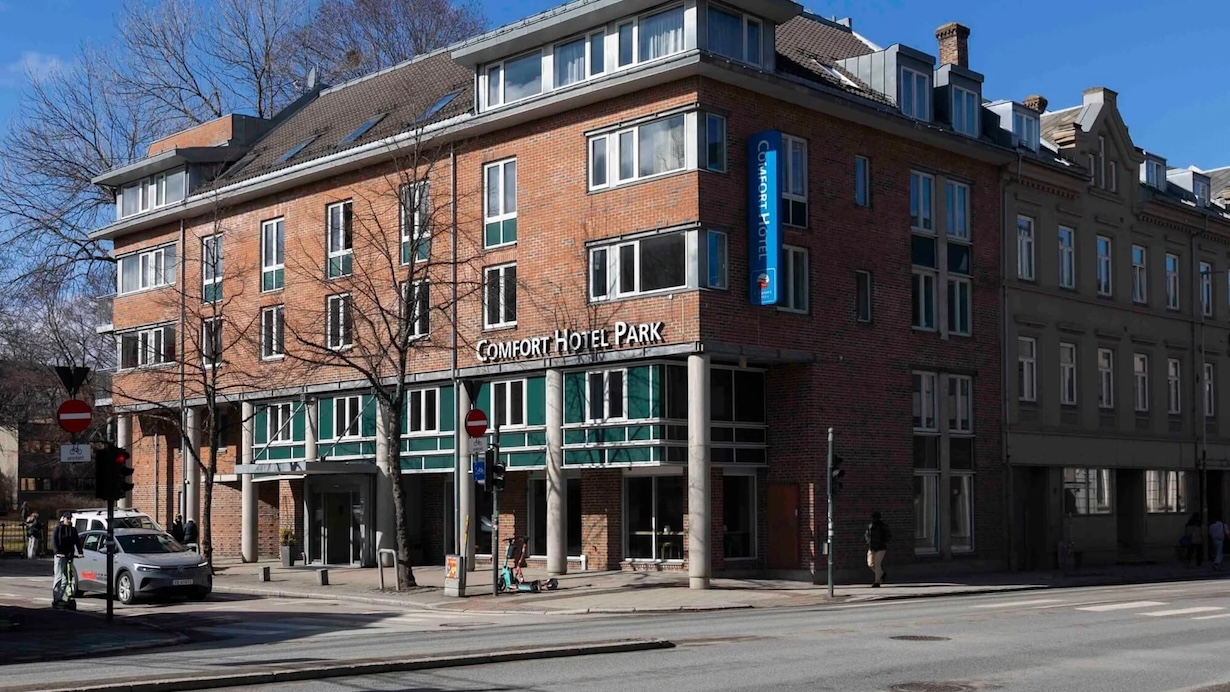 Et bilde av et bygg av mur. På midten av bygget henger et stort opplyst skilt hvor det står Comfort Hotel Park